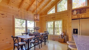 L’intérieur d’un chalet en bois comprend une table à manger, des chaises, un coin cuisine et de grandes fenêtres.