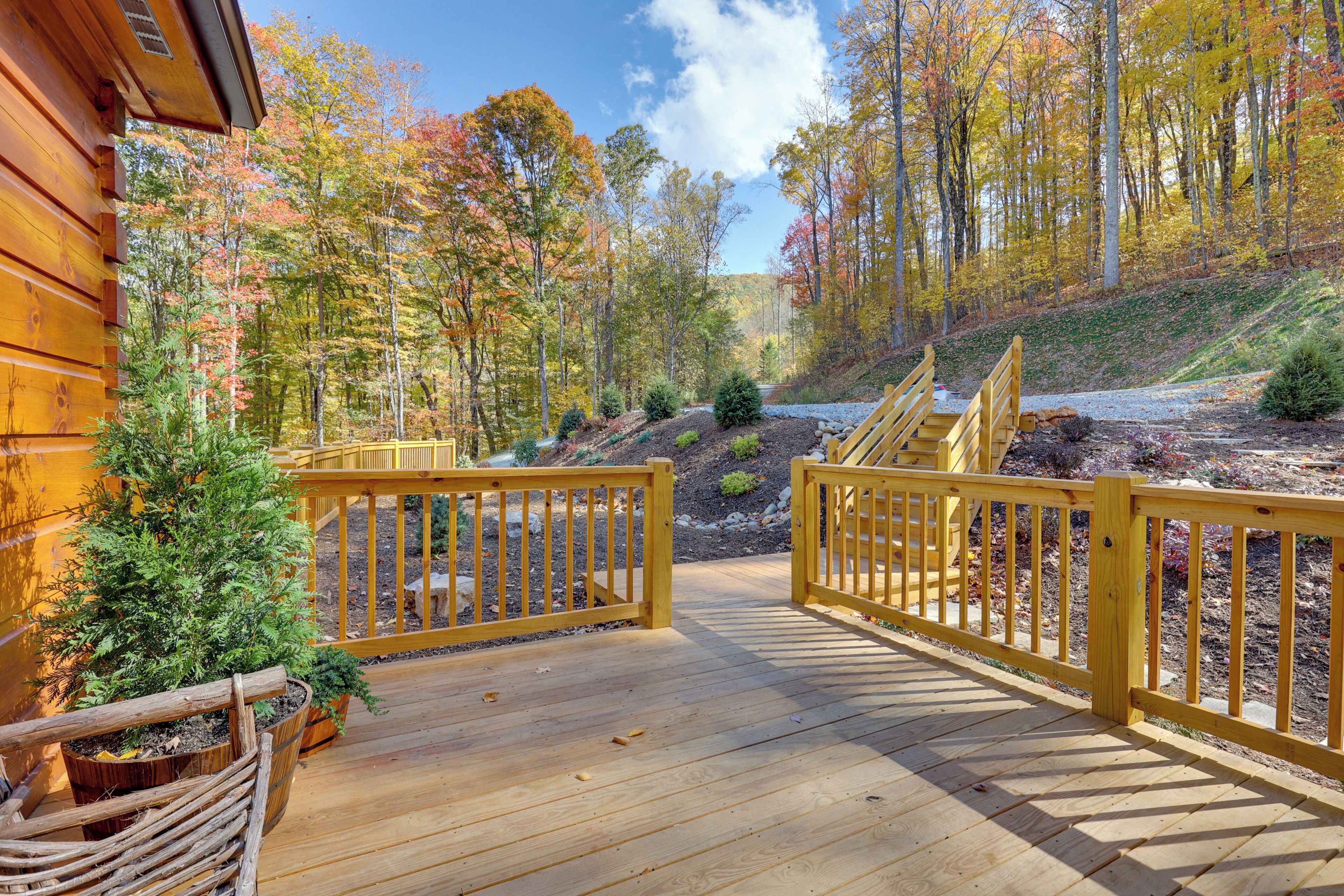 A wooden deck with railings, surrounded by a forest with autumn foliage.