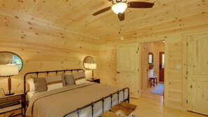 Une chambre dans une cabane en bois, avec un lit, deux tables de chevet, un ventilateur de plafond et une porte en bois.