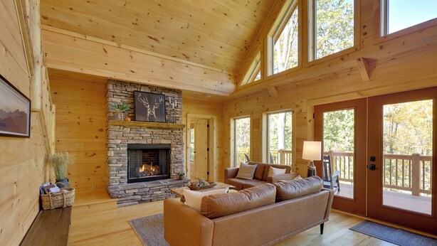 Un intérieur chaleureux de chalet en bois, avec une cheminée en pierre, des planchers en bois et de grandes fenêtres.