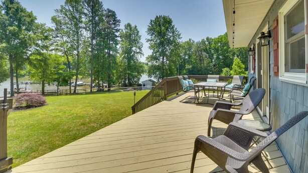 A wooden deck with outdoor furniture, a view of a lake, and a house in the background. - Waterfront, Deck: Peaceful Louisa Cottage Escape (Louisa)