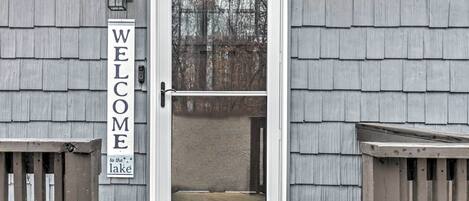 A wooden door with a 'WELCOME to the lake' sign, a small porch, and a wooden fence.