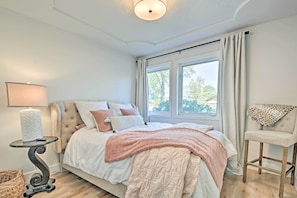 Un dormitorio con cama, mesita de noche con lámpara, una silla y ventana con cortinas.