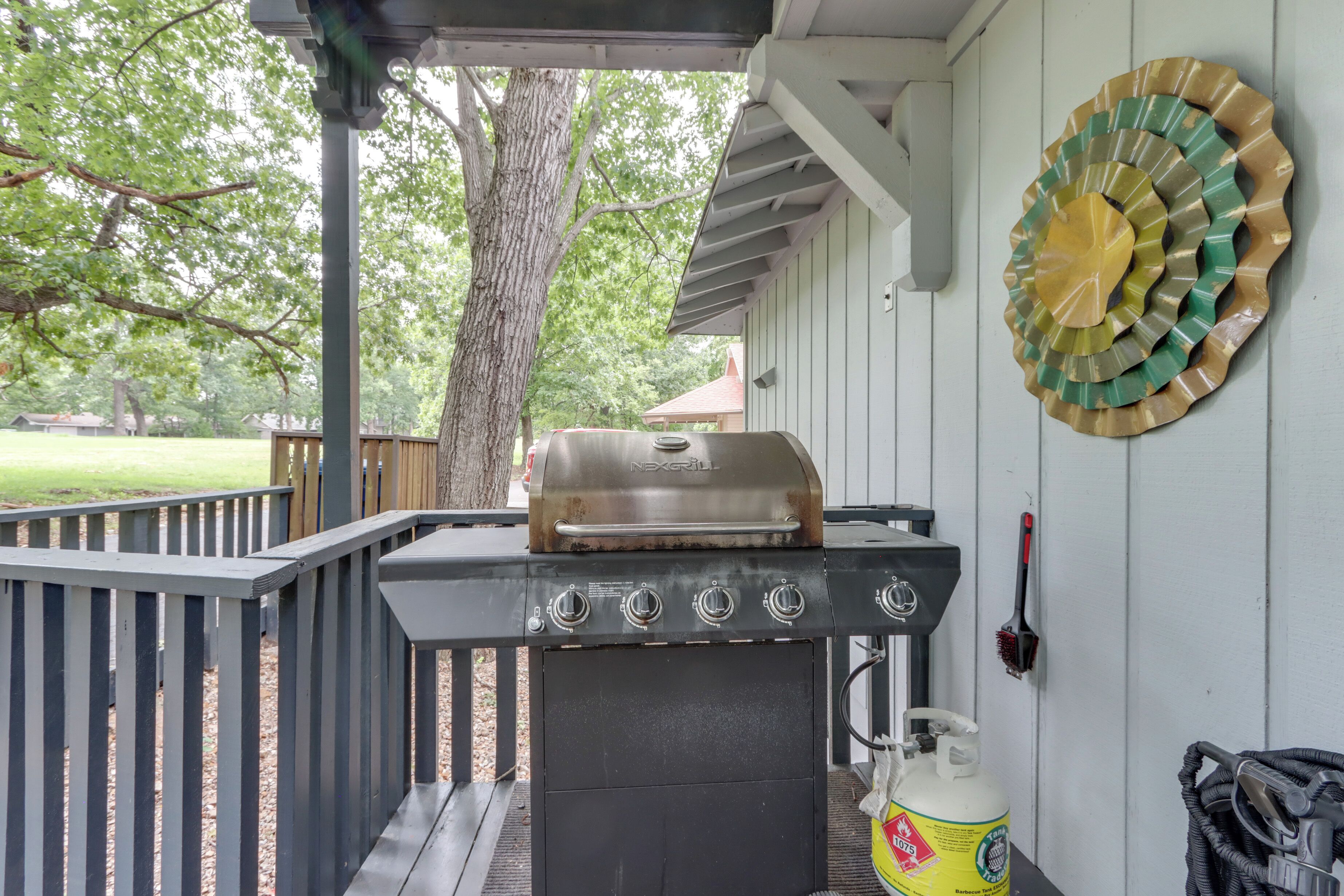 A barbecue grill on an outdoor deck with a tree and a decorative plate in the background.