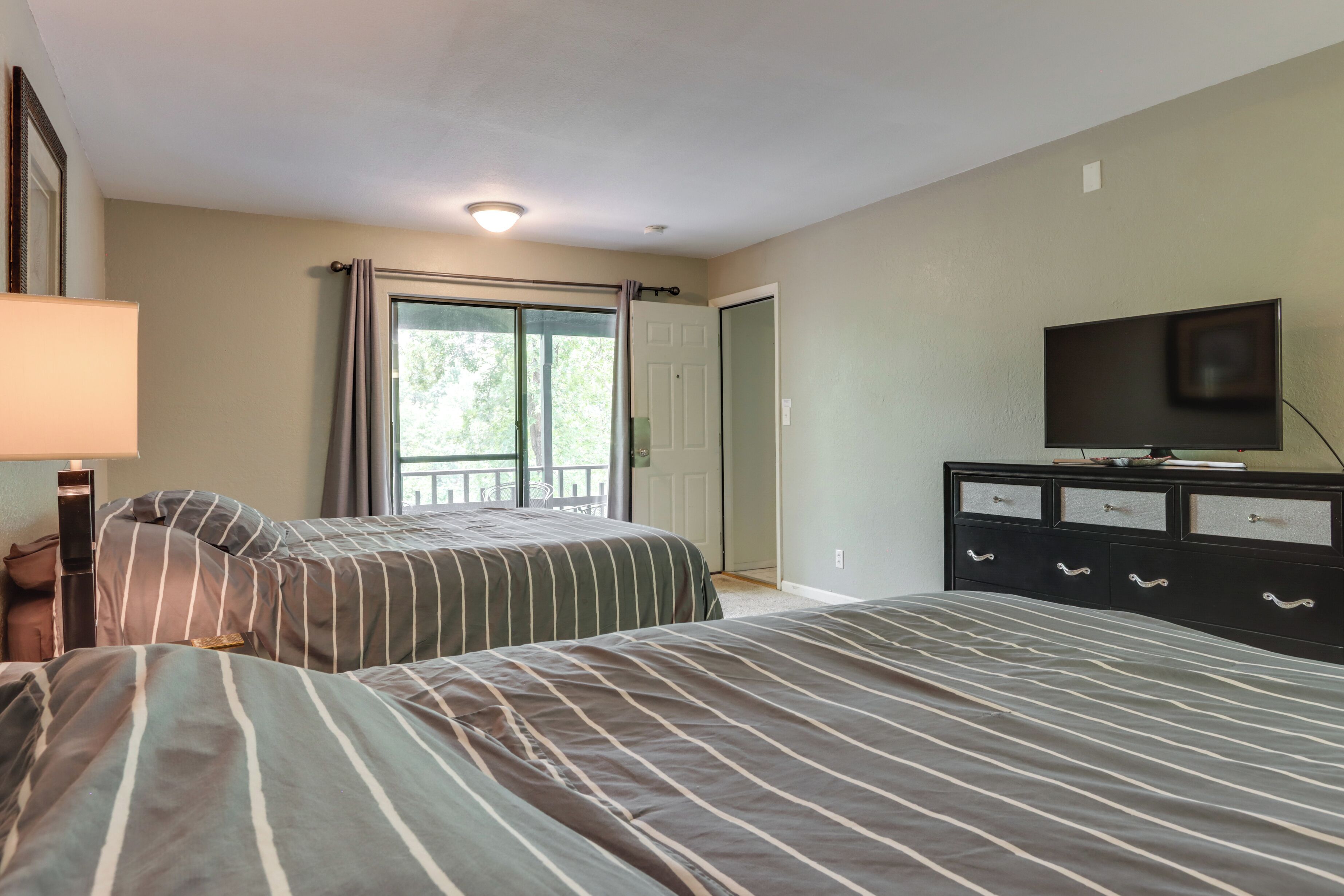 A bedroom with two beds, a TV, a dresser, and a sliding glass door to a balcony.