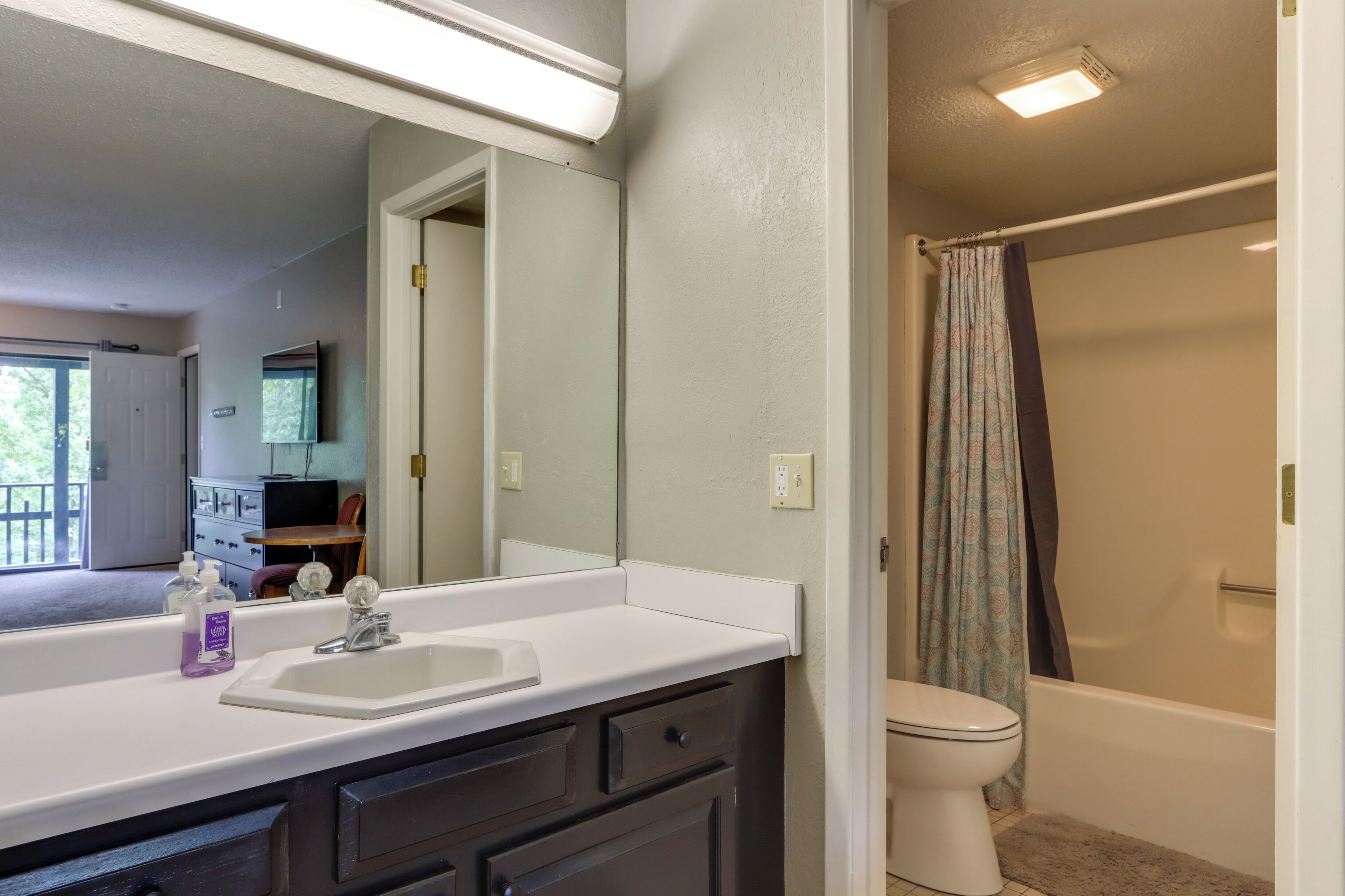 A bathroom with a white sink, dark cabinets, a mirror, a toilet, and a shower curtain.