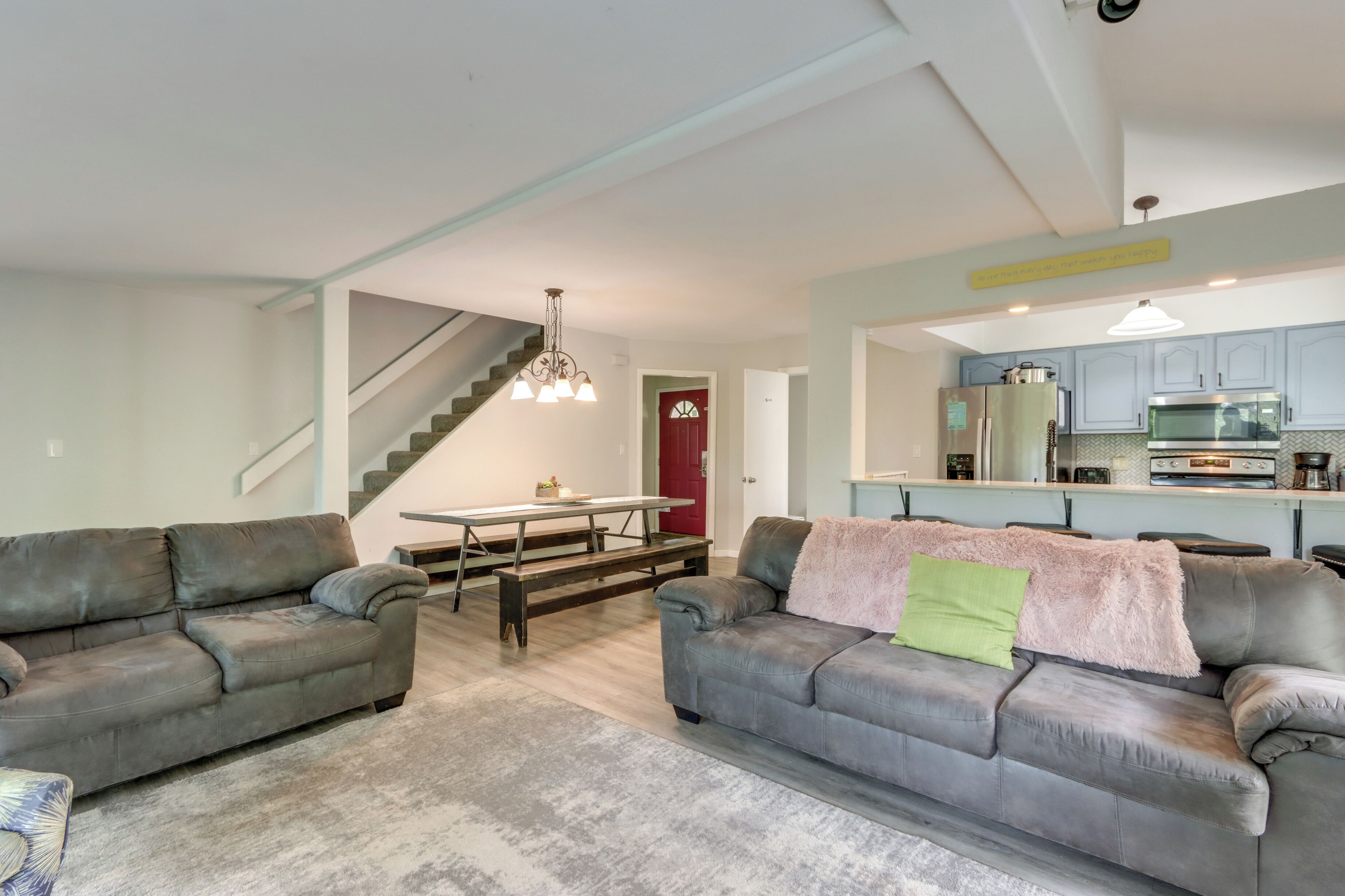 A modern living room with two grey sofas, a wooden dining table, and a staircase leading to another level.