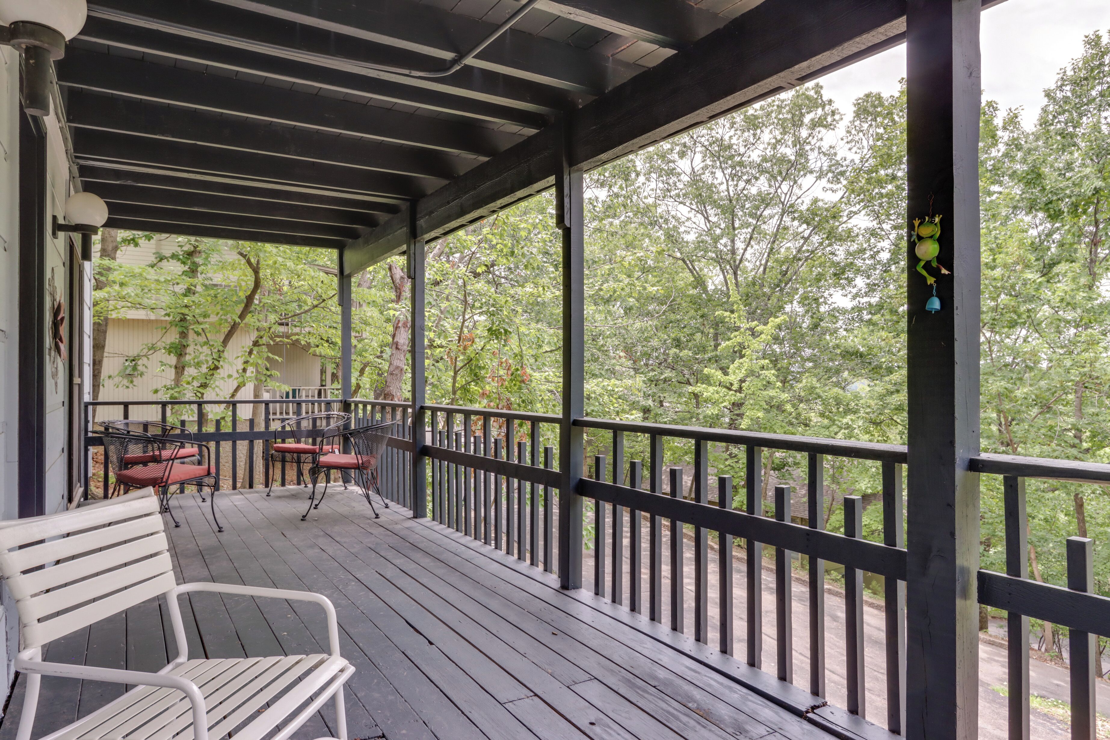 Une véranda couverte avec un banc et des chaises, des balustrades en bois et une vue sur les arbres.