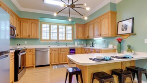 A modern kitchen with wooden cabinets, a large island, and a stainless steel refrigerator. - Chic Home w/ Club Access Near Bay St Louis! (Diamondhead)