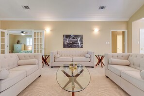 A living room with two beige sofas, a glass coffee table, and a black and white painting on the wall. - Chic Home w/ Club Access Near Bay St Louis! (Diamondhead)