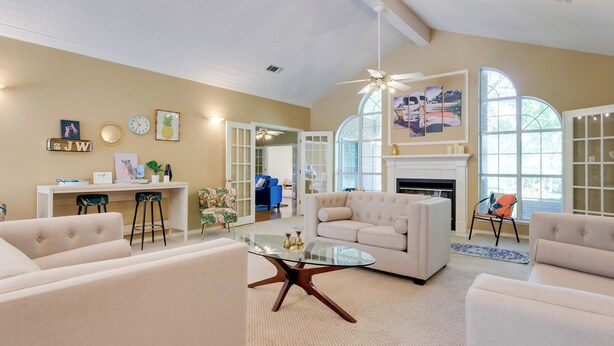 A spacious living room with a large white sofa, a glass coffee table, and a fireplace. There are two chairs, a desk, and a bookshelf in the background. - Chic Home w/ Club Access Near Bay St Louis! (Diamondhead)