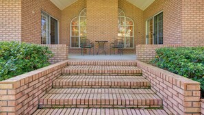 A brick building with a covered porch, two tables, and chairs. - Chic Home w/ Club Access Near Bay St Louis! (Diamondhead)