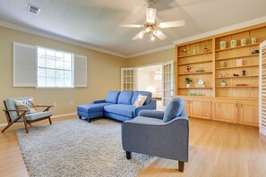 A living room with a sectional sofa, a single armchair, a wooden bookshelf, and a ceiling fan. - Chic Home w/ Club Access Near Bay St Louis! (Diamondhead)