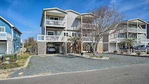 A multi-story residential building with a covered parking area, a fenced front yard, and a gravel driveway.
