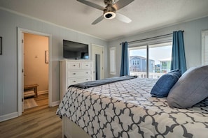 A bedroom with a bed, a ceiling fan, a TV, and a window with curtains. - Holden Beach Vacation Rental: Short Path to Beach! (Supply)