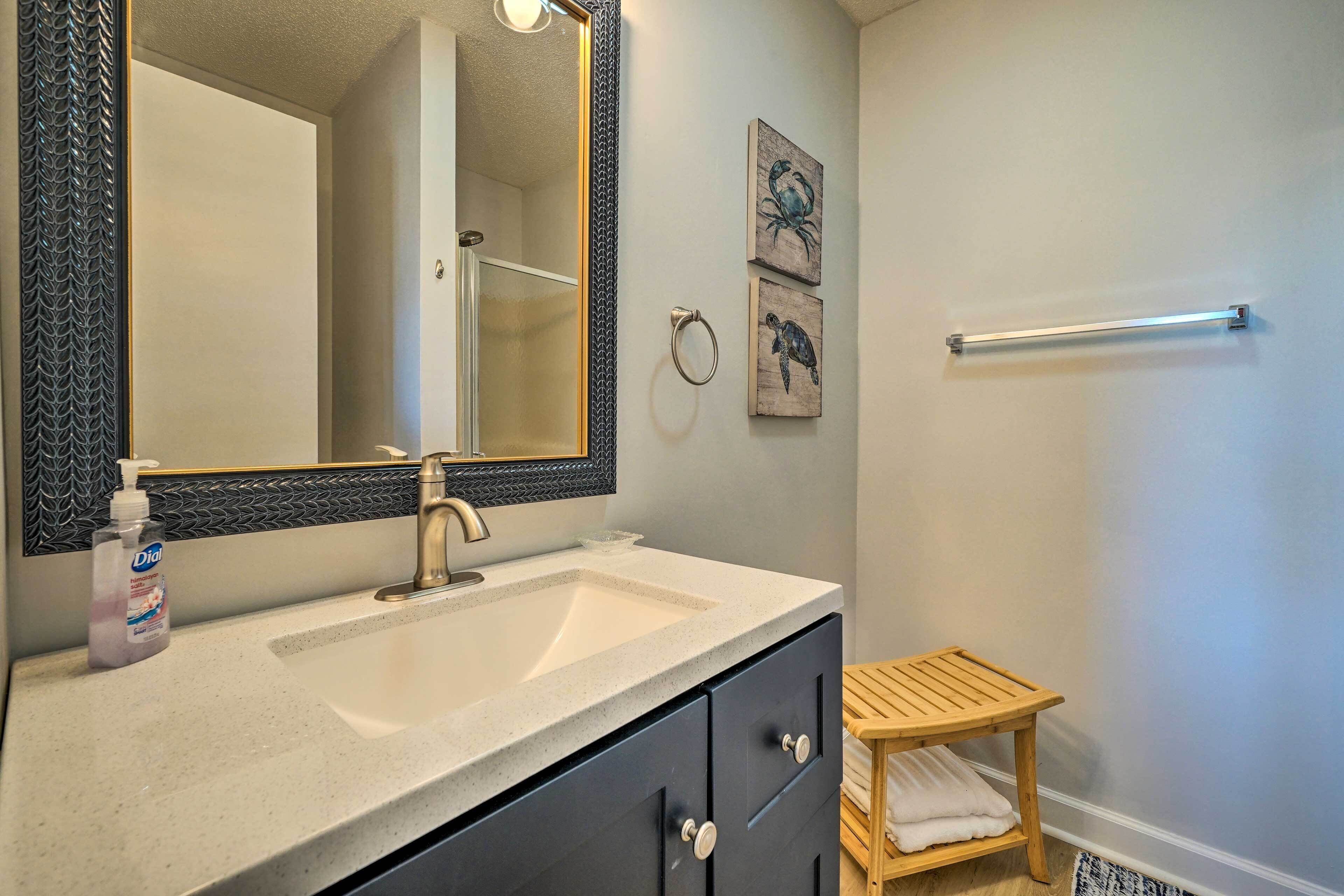 A bathroom with a large mirror, a sink, a wooden stool, and two wall-mounted towel rings.