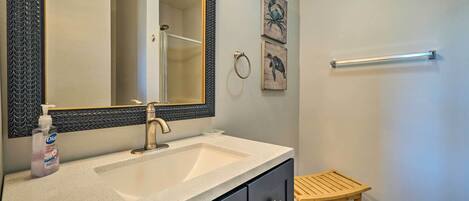A bathroom with a large mirror, a sink, a wooden stool, and two wall-mounted towel rings.