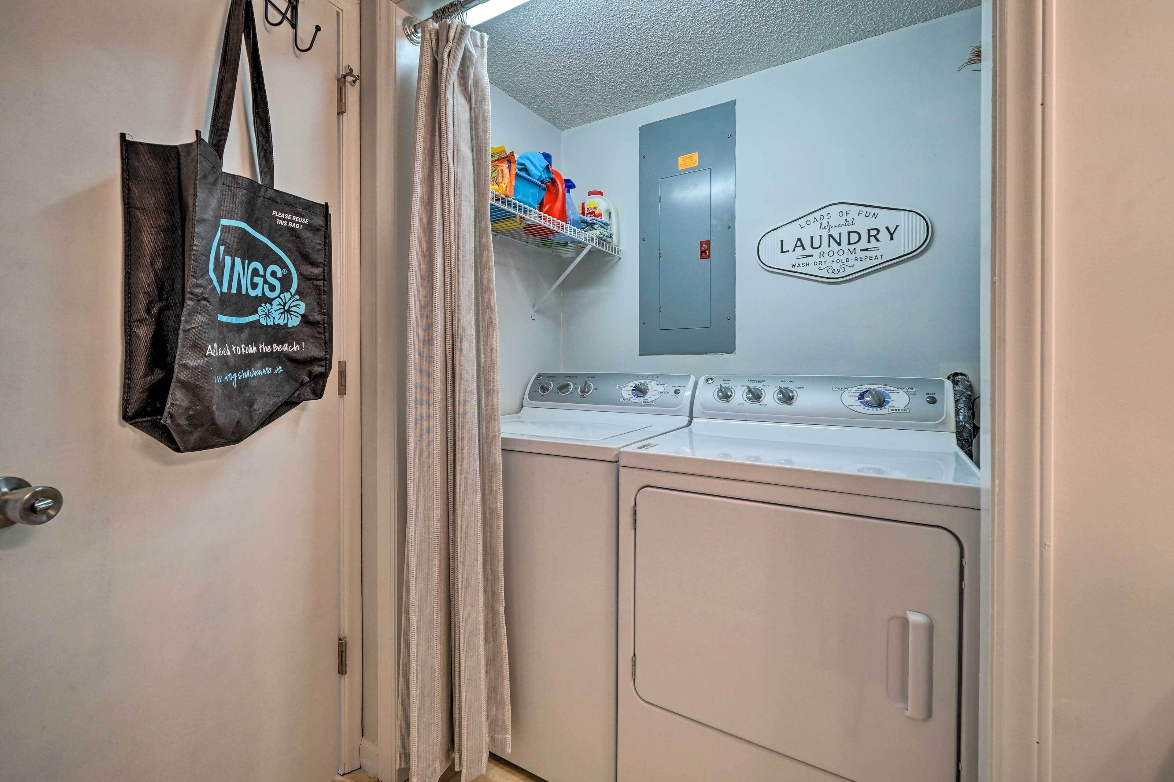 A laundry room with a washing machine, a dryer, and a shelf with cleaning supplies. A black tote bag hangs on the door.