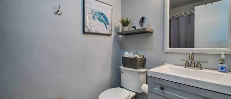 Une salle de bain équipée de toilettes, d’un lavabo, d’un miroir et d’un tableau encadré accroché au mur.