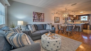 A modern living room with a gray sofa, ottoman, and dining area with wooden chairs.