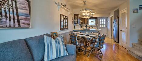 A modern kitchen with a dining area, wooden flooring, and a gray sofa with striped pillows.