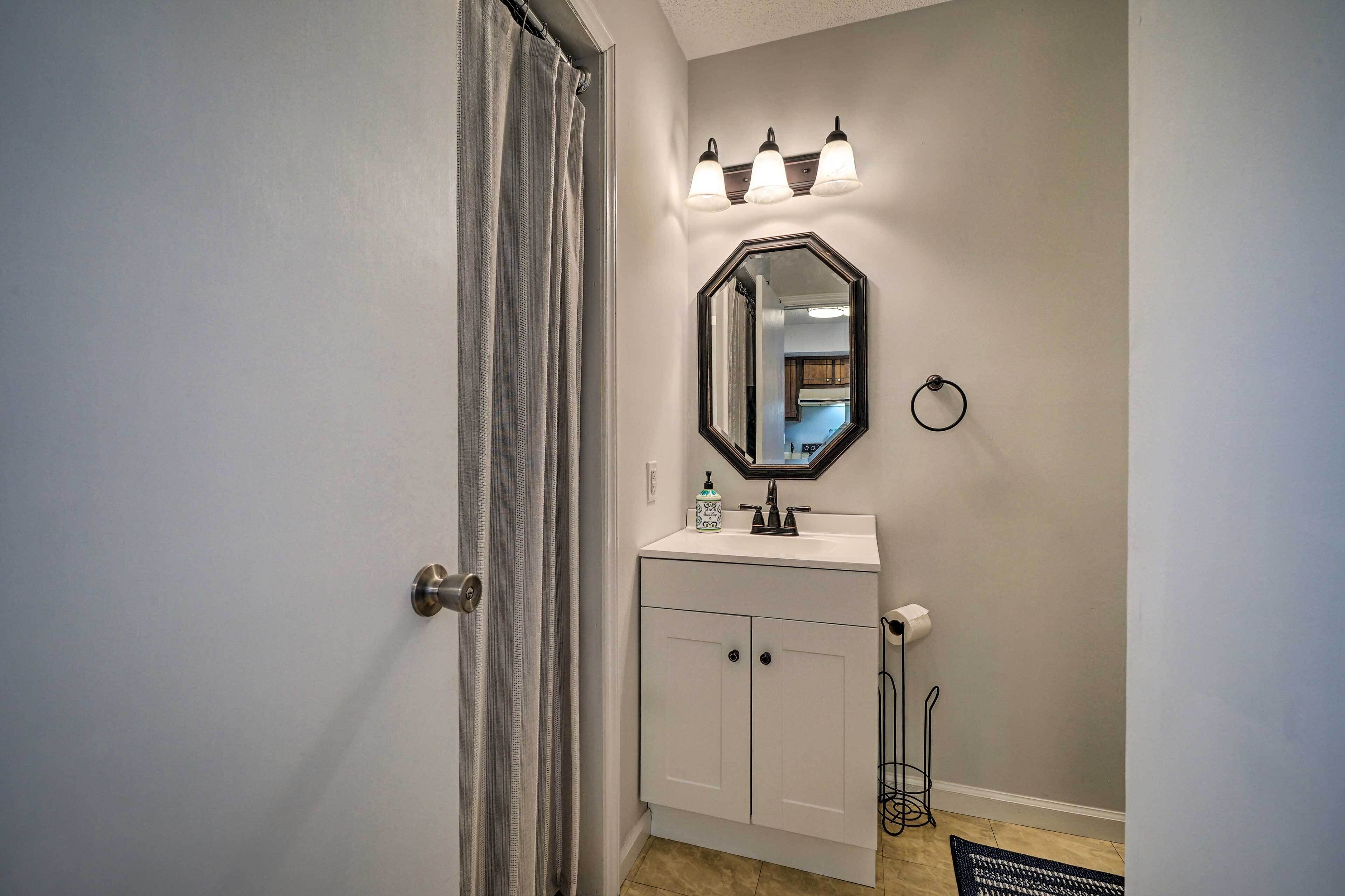 A bathroom with a white vanity, a mirror with lights, a towel ring, and a toilet paper holder.