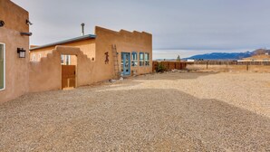 A building with a gravel driveway, a blue door, and a ladder leaning against the wall. - Ideally Located Taos Vacation Rental w/ Gas Grill (Ranchos De Taos)