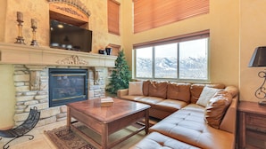 A living room with a stone fireplace, leather sofa, and a large window with a mountain view. - Eden Townhome w/ Mtn View + Shuttle to Powder Mtn! (Eden)