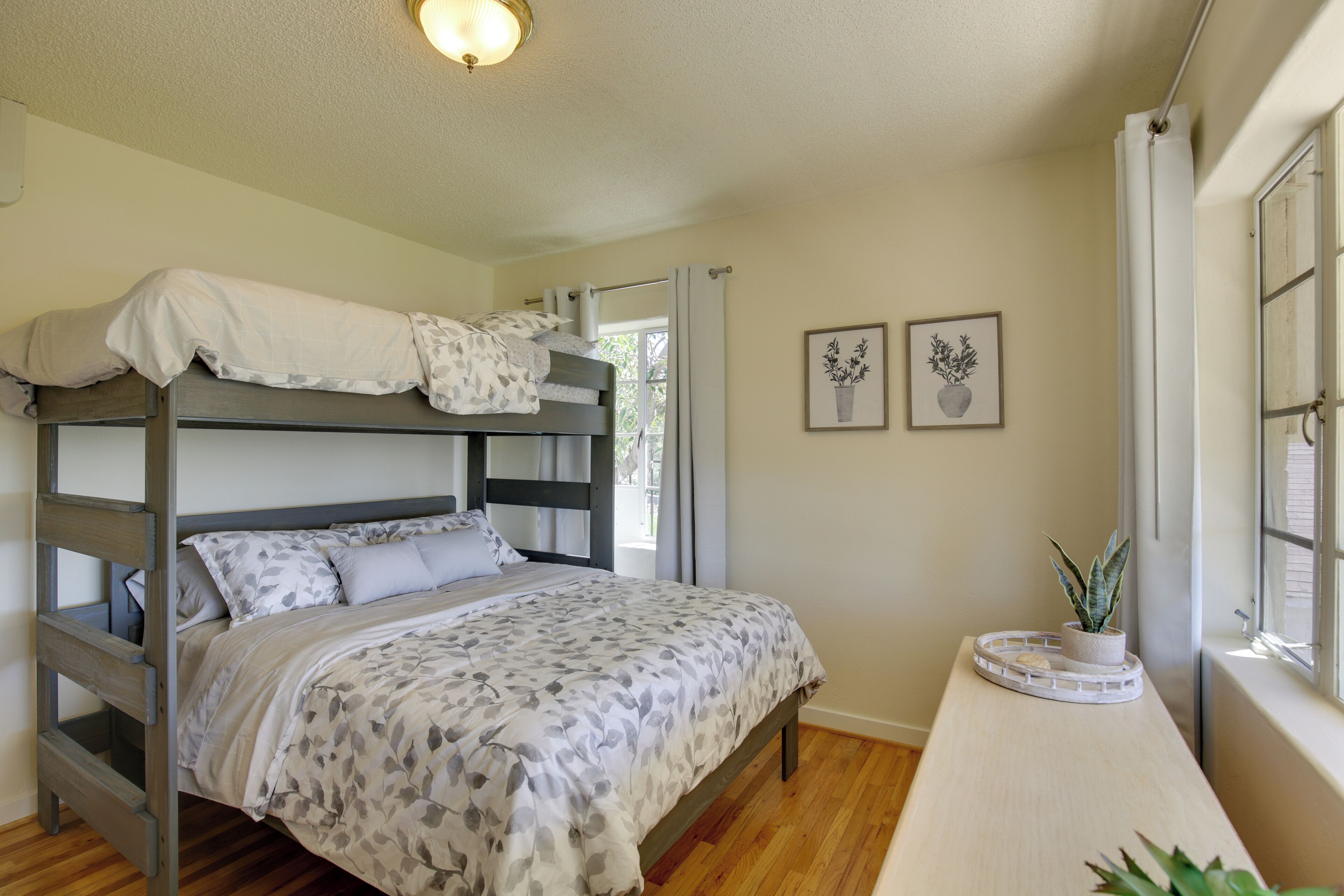 A bunk bed with a floral bedspread, a bedside table with a potted plant, and two framed pictures on the wall.