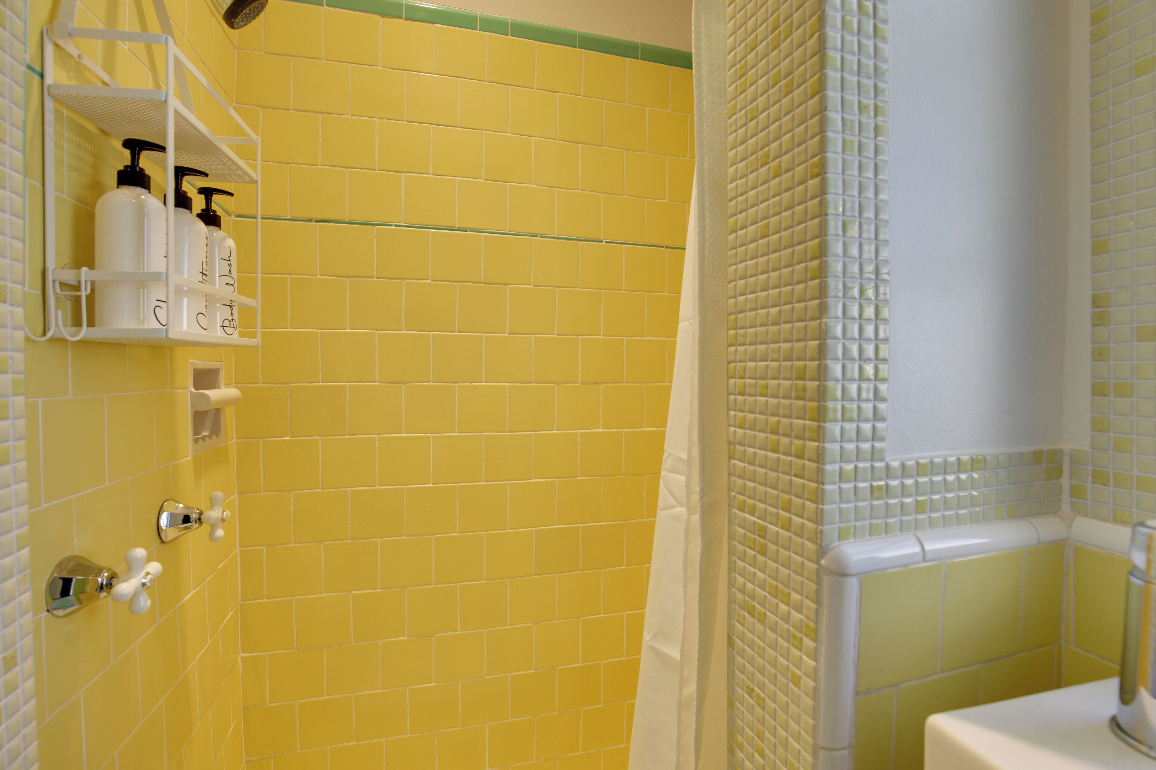 Une salle de bain avec des murs recouverts de carreaux jaunes, un espace douche et un lavabo blanc.