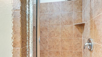 A bathroom with beige tiles, a showerhead, and a corner sink.