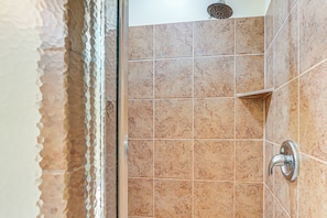 Een badkamer met beige tegels, een douchekop en een wastafel in een hoek.