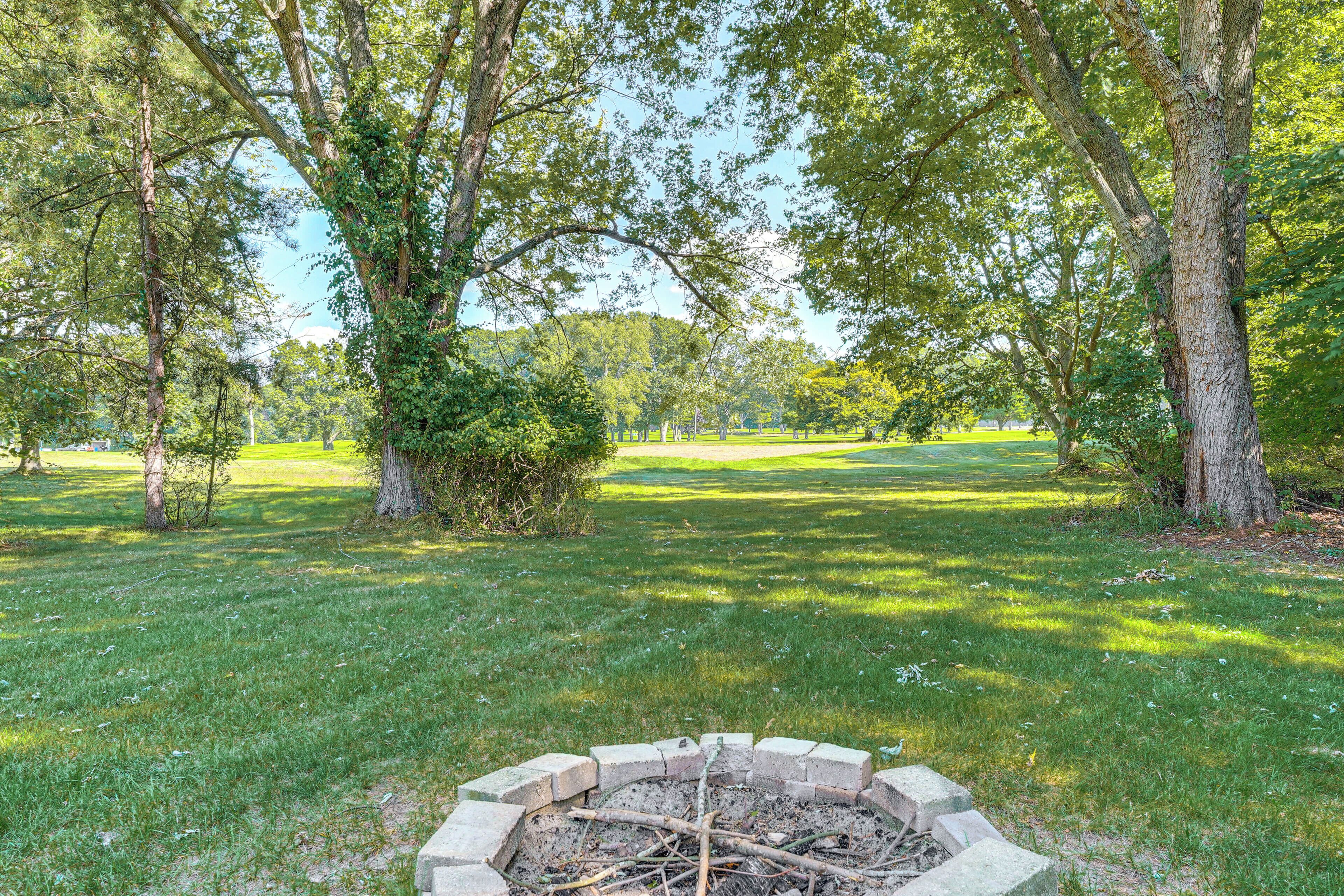A fire pit surrounded by grass and trees in a park setting.