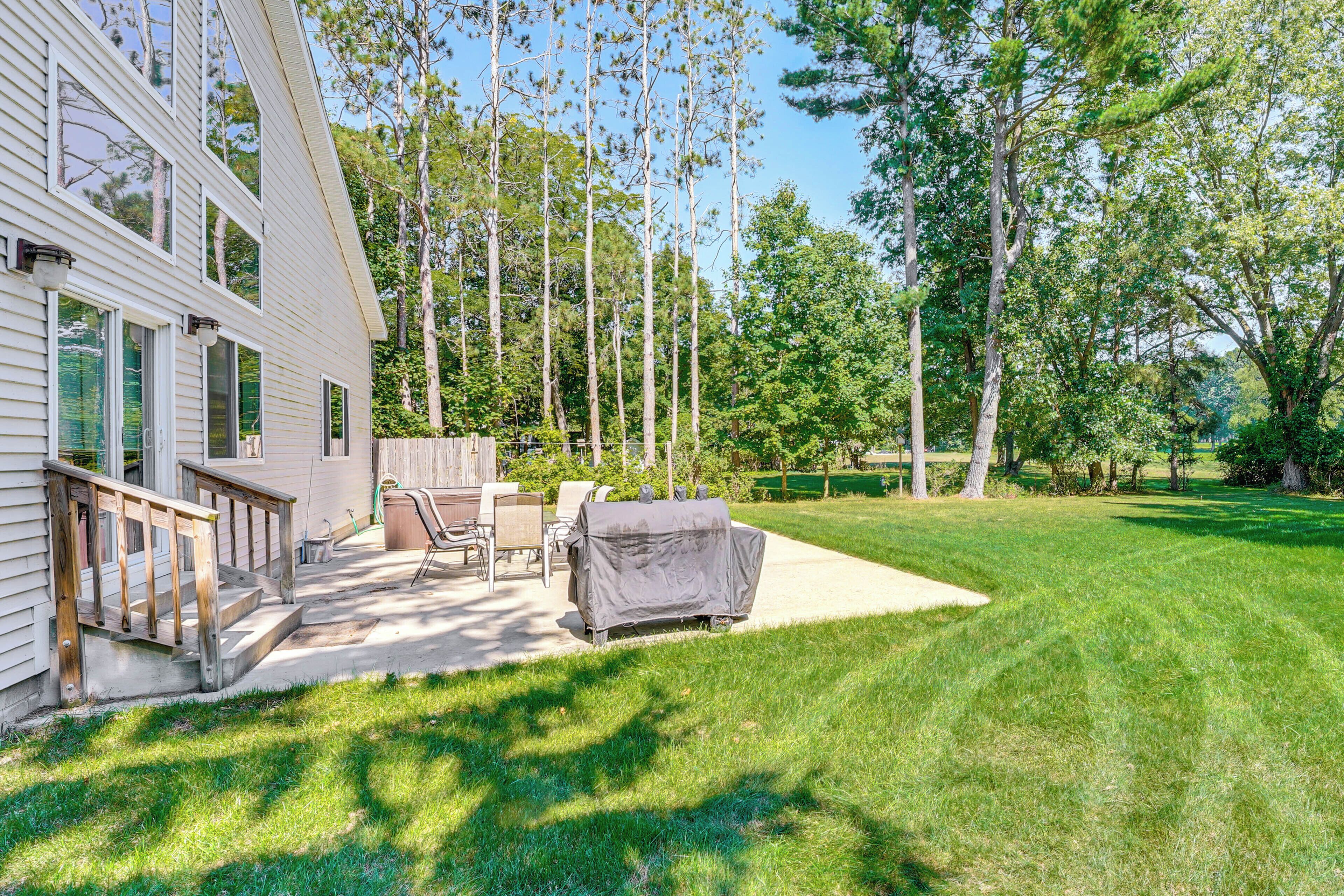 A backyard with a covered grill, outdoor furniture, and a wooden deck leading to a house.