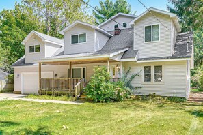A two-story house with a covered porch, a garage, and a small front yard with a wooden deck. - Spacious Whitehall Home w/ Hot Tub: Walk to Beach! (Whitehall)