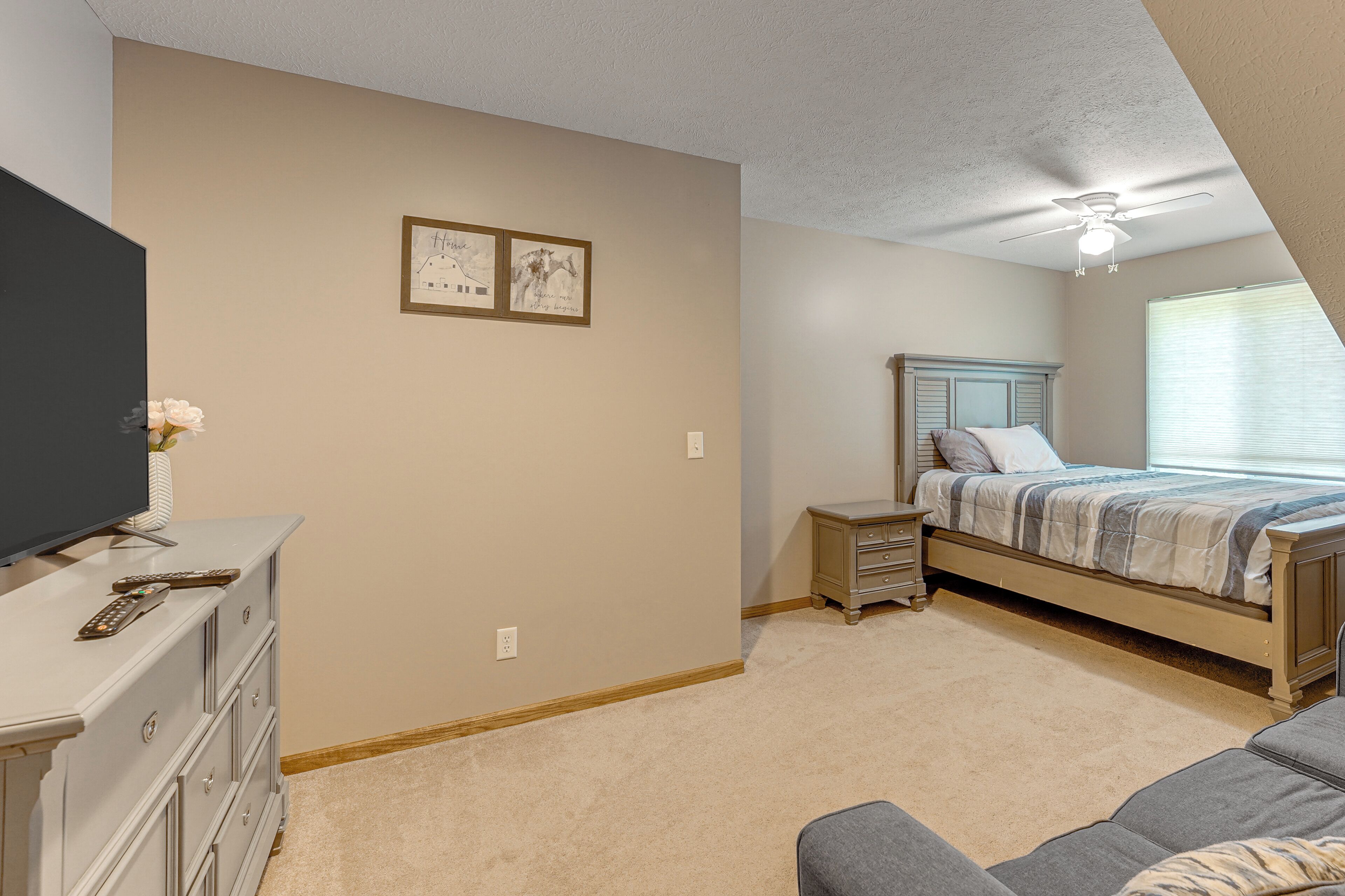A bedroom with a bed, dresser, TV, and ceiling fan.