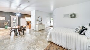 A spacious living area with a dining table, a large bed with striped bedding, and a kitchen in the background.