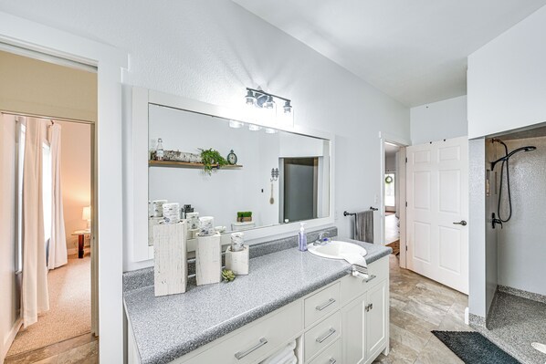 A bathroom with a large mirror, a sink, and a shower area. - Shipshewana Guest House With Fire Pit! (Shipshewana)