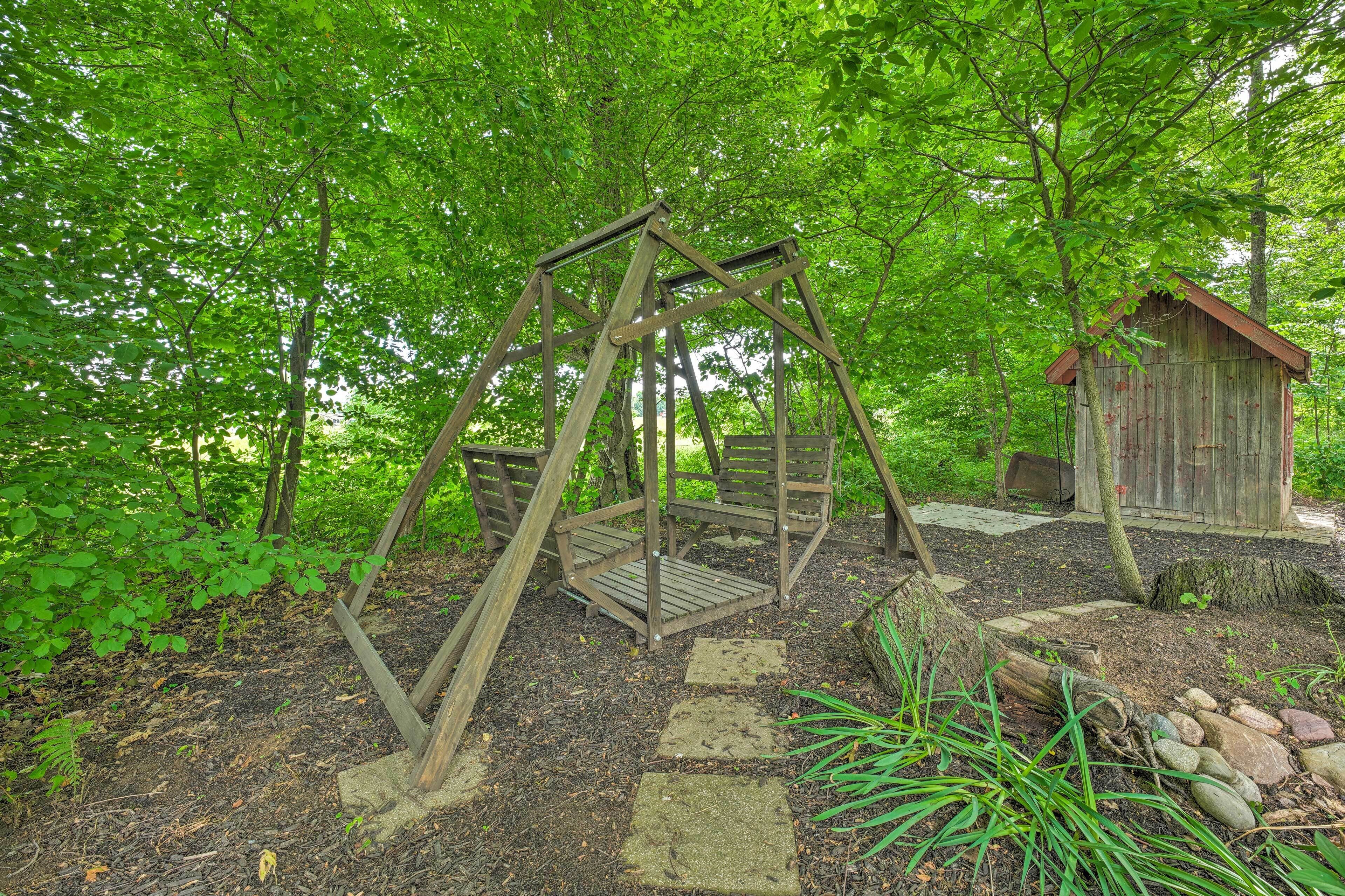 A wooden swing set and a rustic wooden structure in a wooded area.