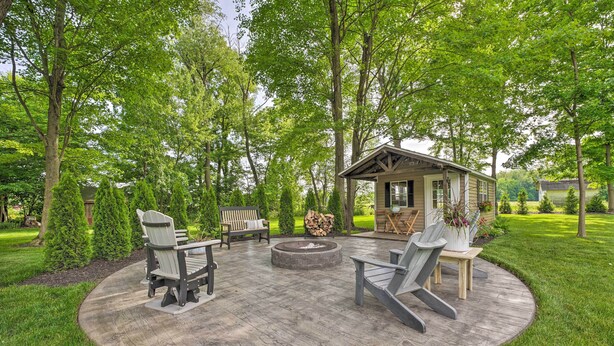 A wooden deck with outdoor furniture, a fire pit, and a small cabin-like structure surrounded by lush greenery.