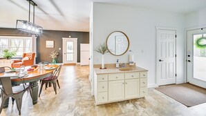 A modern kitchen with a dining area, a large window, and a white door with a wreath.