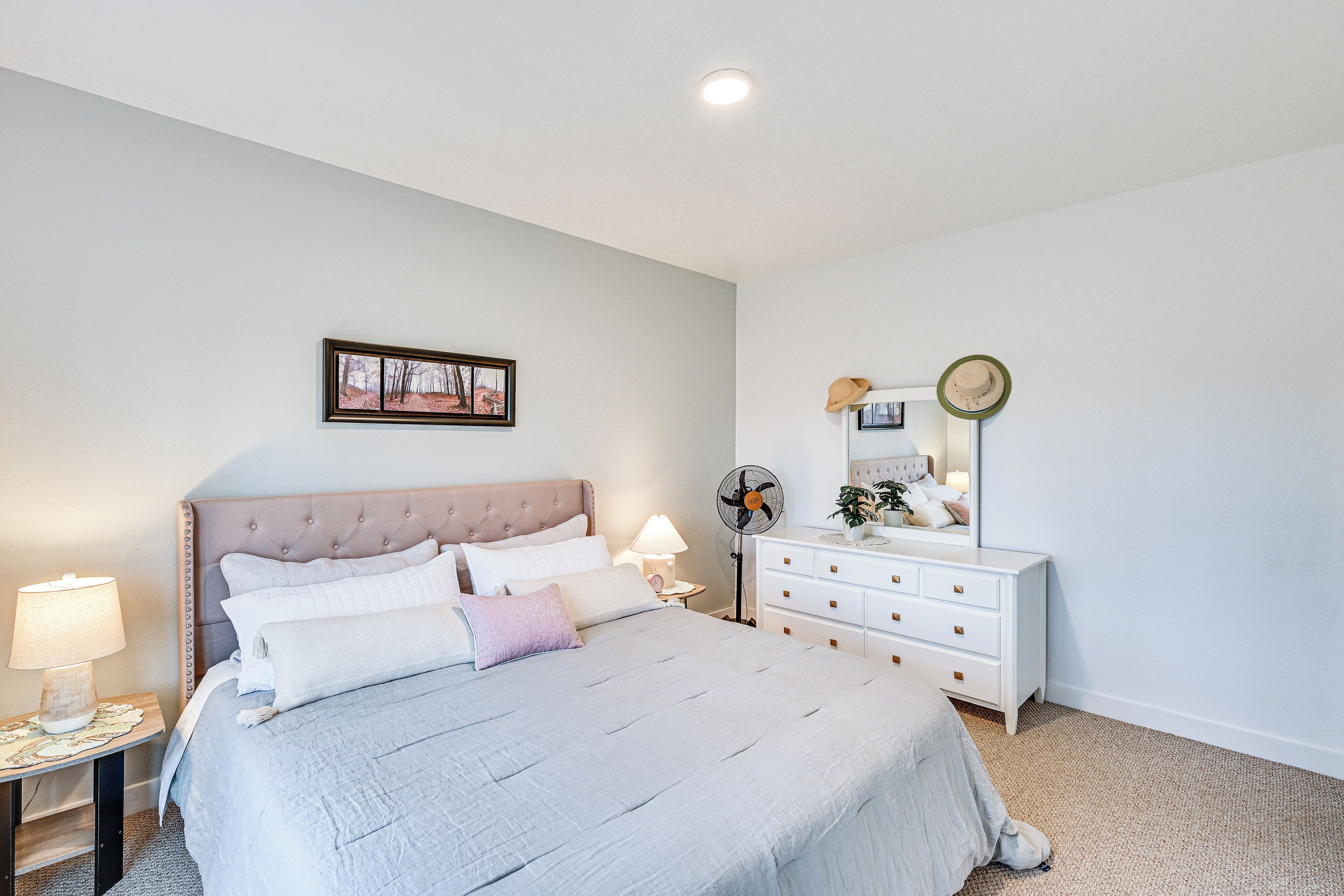 A neatly arranged bedroom with a bed, bedside tables, a dresser, and a mirror.