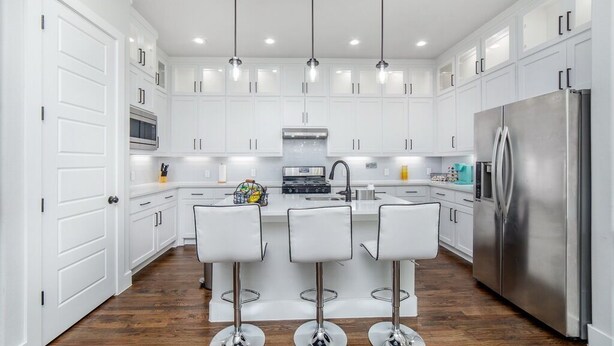 A modern kitchen with white cabinets, stainless steel appliances, and three bar stools. - Glam Paradaise 5BRs Home in Downtown Dallas (Dallas)