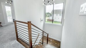 A staircase with a wooden handrail and metal balusters, leading to a room with a large window and a view of a house outside. - Glam Paradaise 5BRs Home in Downtown Dallas (Dallas)