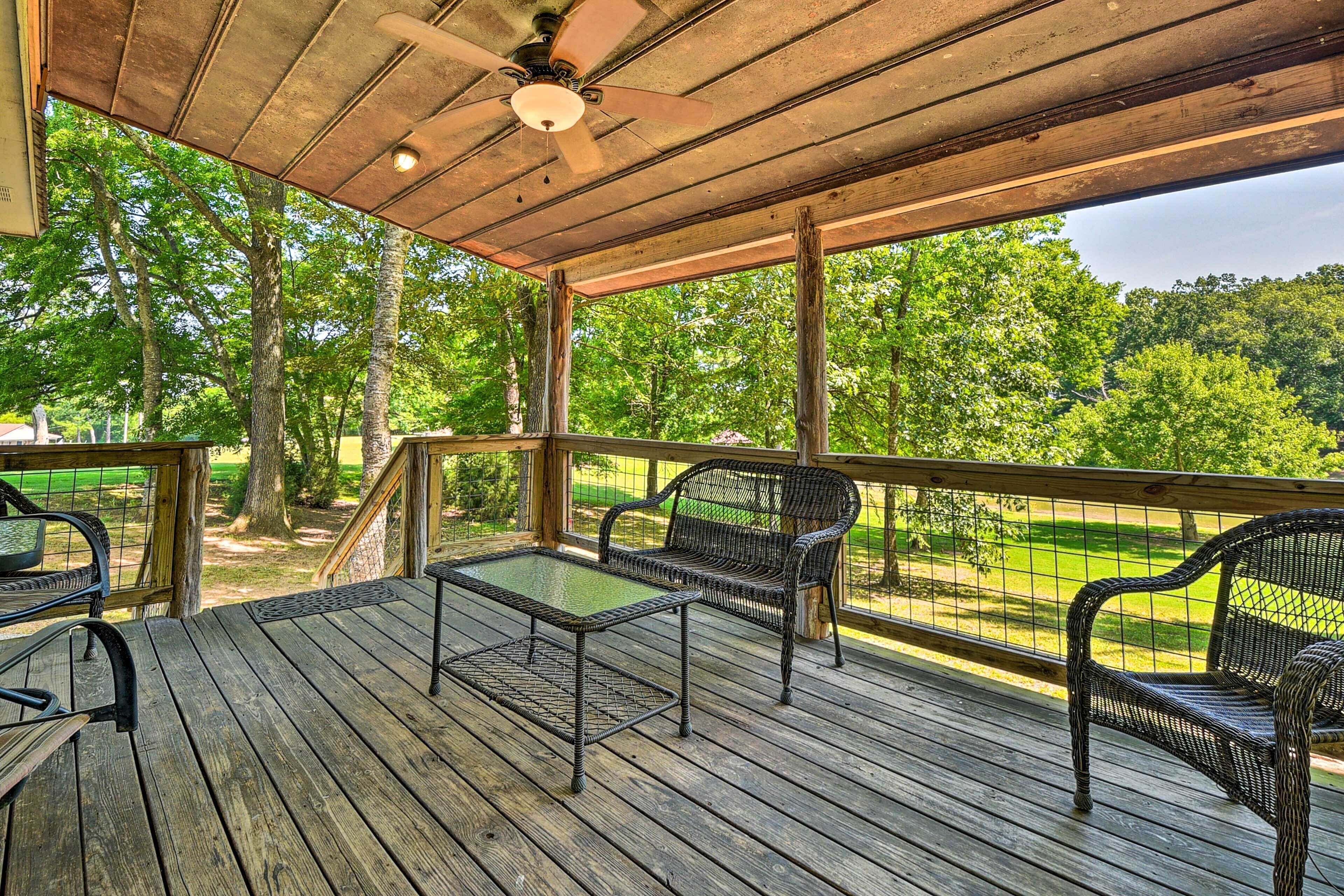 A wooden deck with a table and two chairs, overlooking a green landscape.