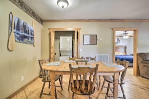 Uma sala de jantar com mesa e cadeiras de madeira, uma cozinha com micro-ondas e uma sala de estar com sofá.
