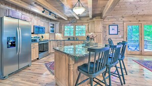 A spacious kitchen with wooden cabinets, a stainless steel refrigerator, a microwave, and a large island with bar stools.