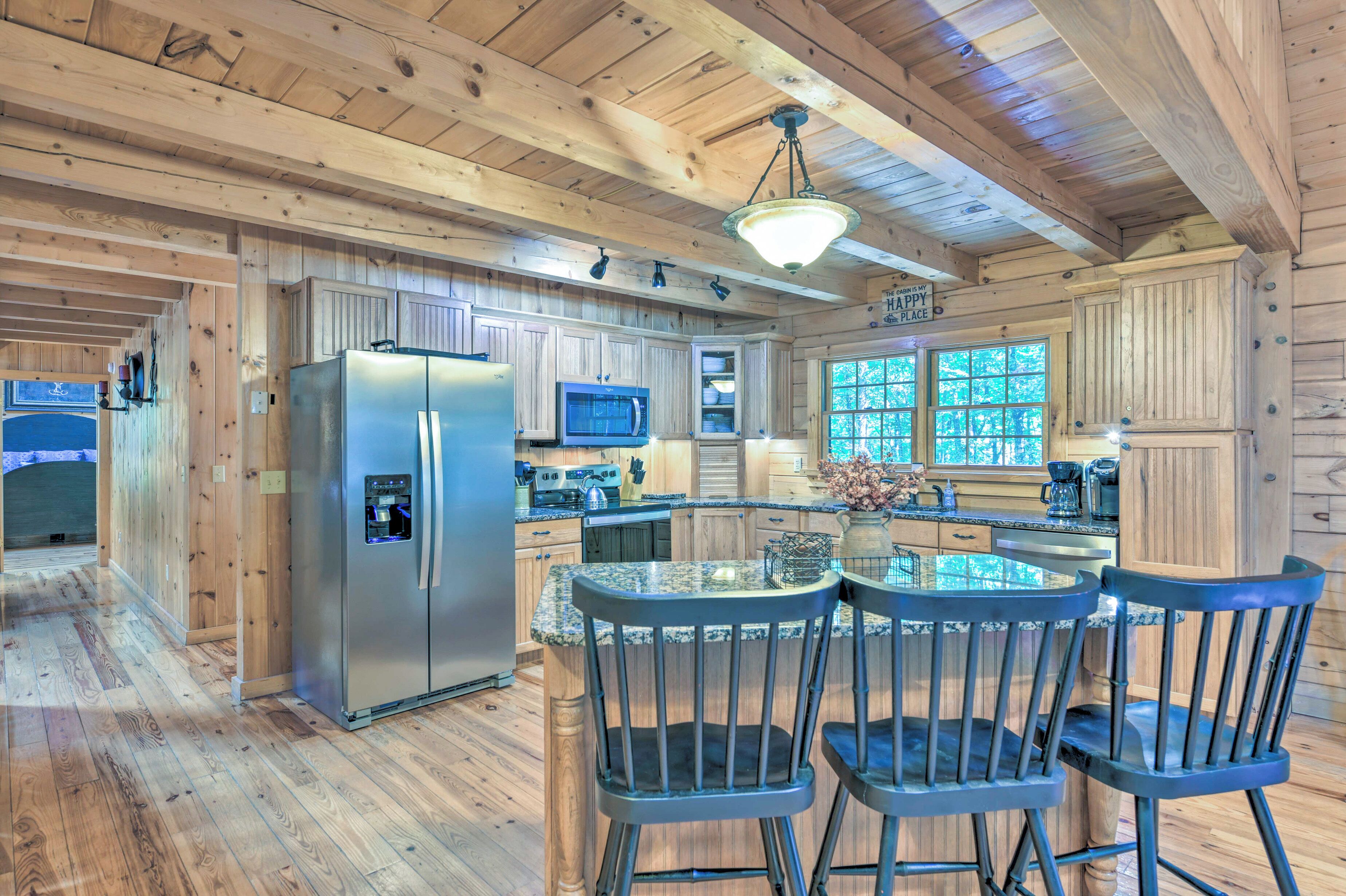 Interior de una cabaña de madera con cocina equipada, que incluye un refrigerador, microondas y armarios de madera. Hay un comedor con mesa y sillas.