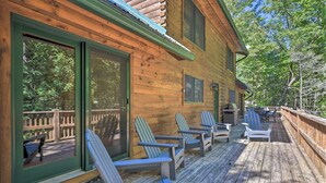 A wooden cabin with a deck, sliding glass doors, and Adirondack chairs.
