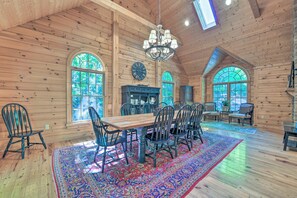 A wooden cabin interior with a dining area, large windows, and a chandelier.